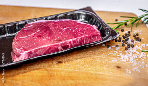 Beef steak in vacuum skin packaging and spices on wooden chopping board with copyspace