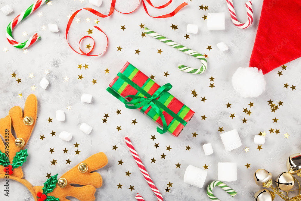 Christmas composition. Gifts, caramel cane, marshmellow, santa hat, headband antlers on gray concrete background with sparkling stars. Concept of winter holidays. Top view