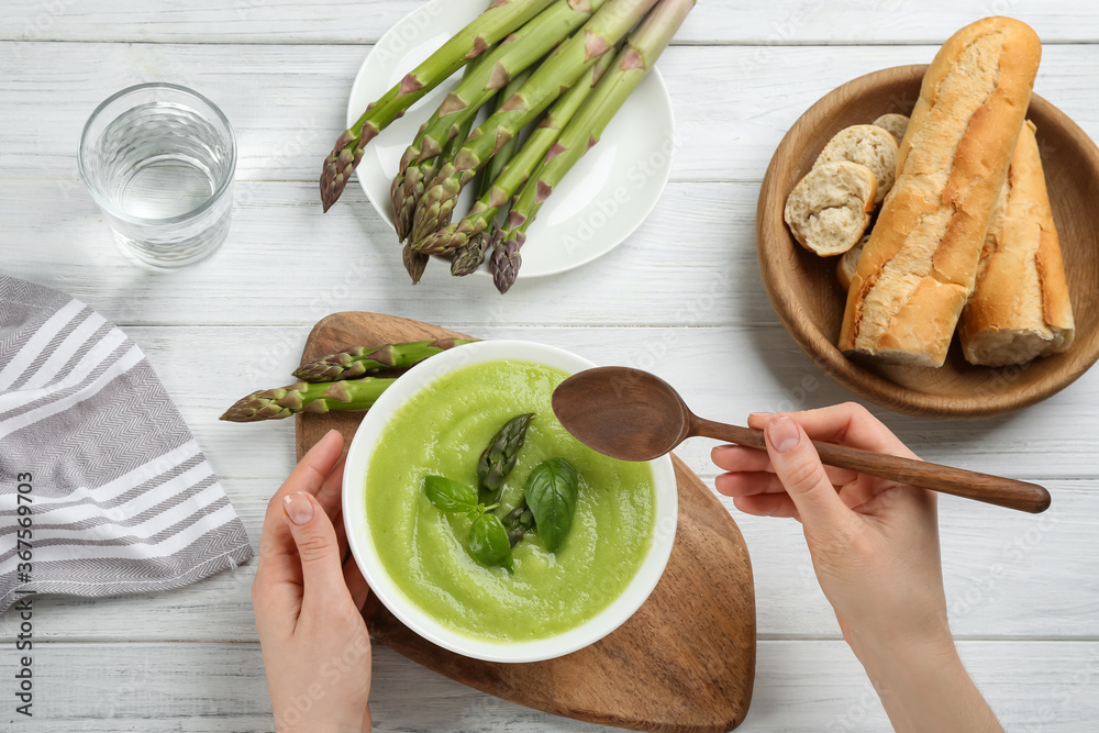 Woman eating delicious asparagus soup at white wooden table, top view - obrazy, fototapety, plakaty 