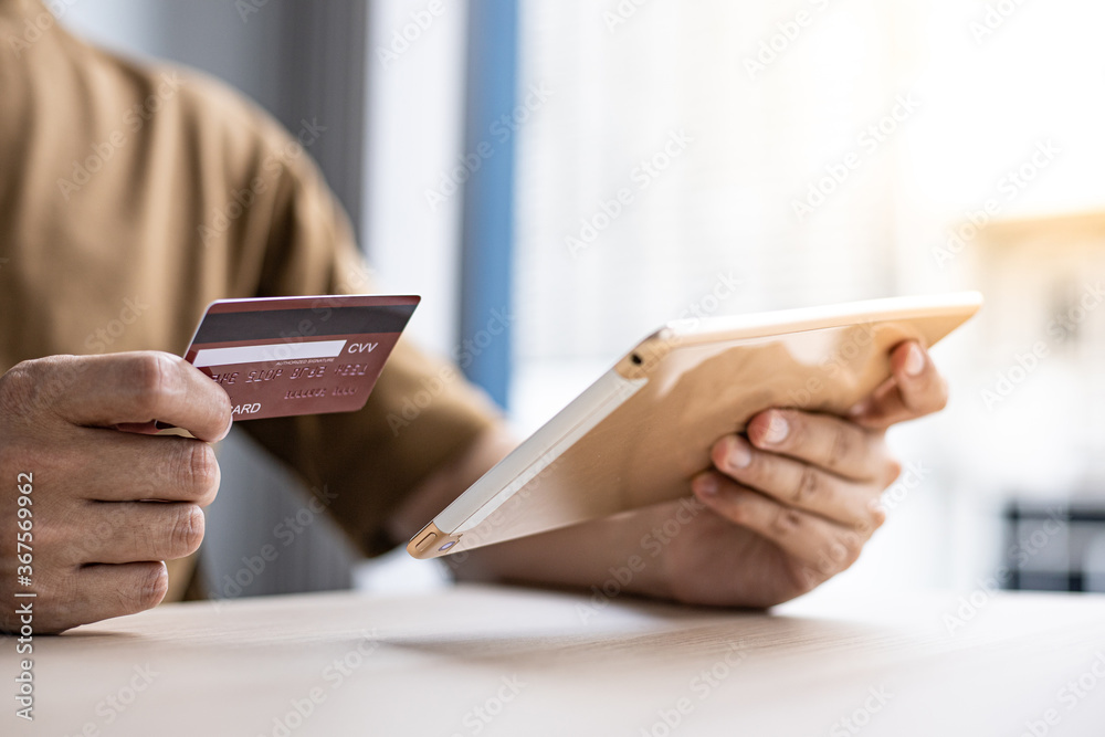 Asian man is holding a credit card and paying with a tablet. Asian man is holding a credit card and paying with a tablet.