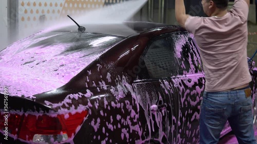 The man washes the car. Washes away pink foam with high pressure water