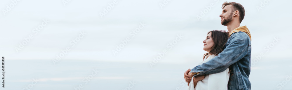panoramic shot of happy man hugging cheerful girlfriend panoramic shot of happy man hugging cheerful girlfriend
