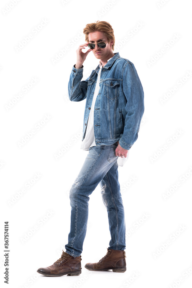 Serious displeased young stylish man in jeans looking above the glasses at camera with strict look. Full body length isolated on white background. Serious displeased young stylish man in jeans looking above the glasses at camera with strict look. Full body length isolated on white background.