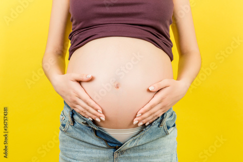 Close up of naked pregnant woman's belly wearing opened jeans at colorful background with copy space. Pregnancy concept © sosiukin