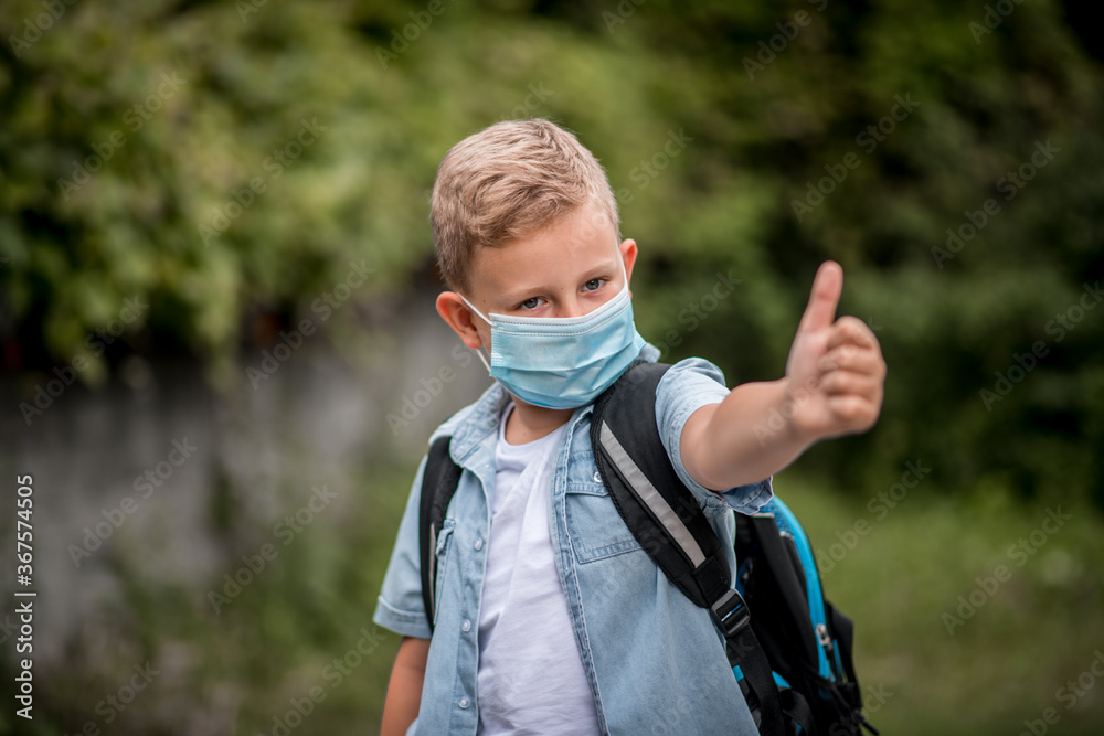 Caucasian schoolboy wearing mask and giving thumb up, school reopening, return back to school after  corona virus pandemic is over, new normal concept