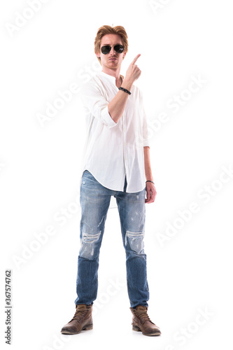 Confident successful young stylish man advertising and pointing finger upwards at side. Full body length isolated on white background.  © sharplaninac