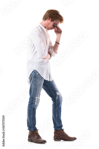 Sad concerned young handsome man looking down thoughtful. Side view. Full body length isolated on white background. 