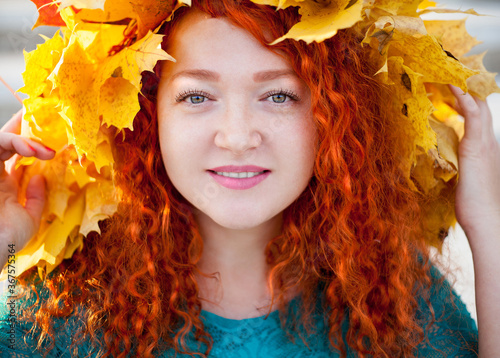 Portrait of a young woman with red hair in a wreath of maple leaves