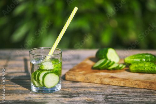 refreshing water lemonade from cucumbers in glass with drinking straw. sliced fresh cucumbers on wooden board. summer cocktail