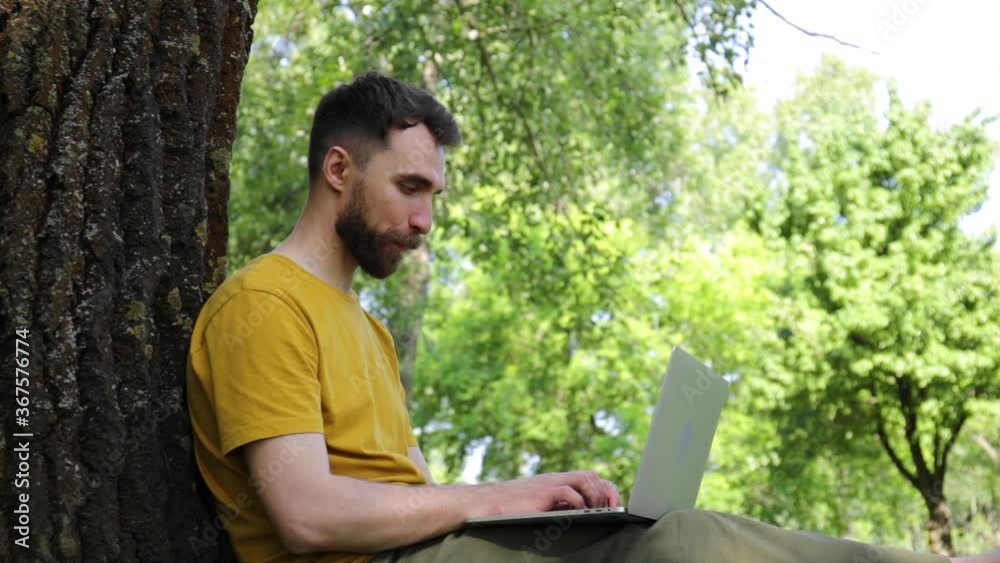 happy freelancer sitting near tree trunk with laptop happy freelancer sitting near tree trunk with laptop