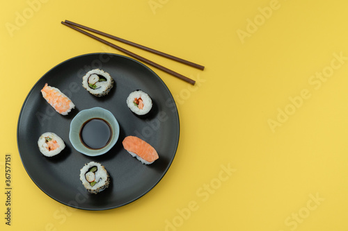 Dish with Sushi and chopsticks on a yellow background Copy space.