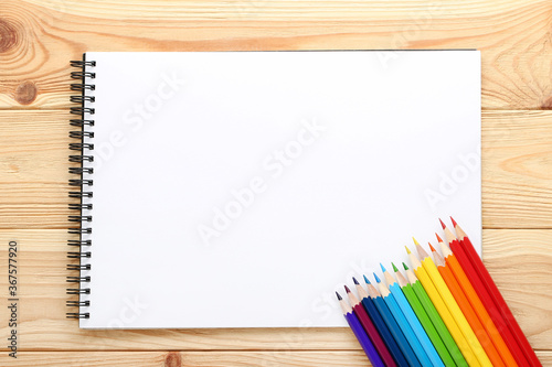 Colored pencils with notebook on brown wooden table