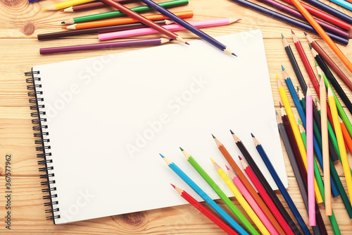 Colored pencils with notebook on brown wooden table