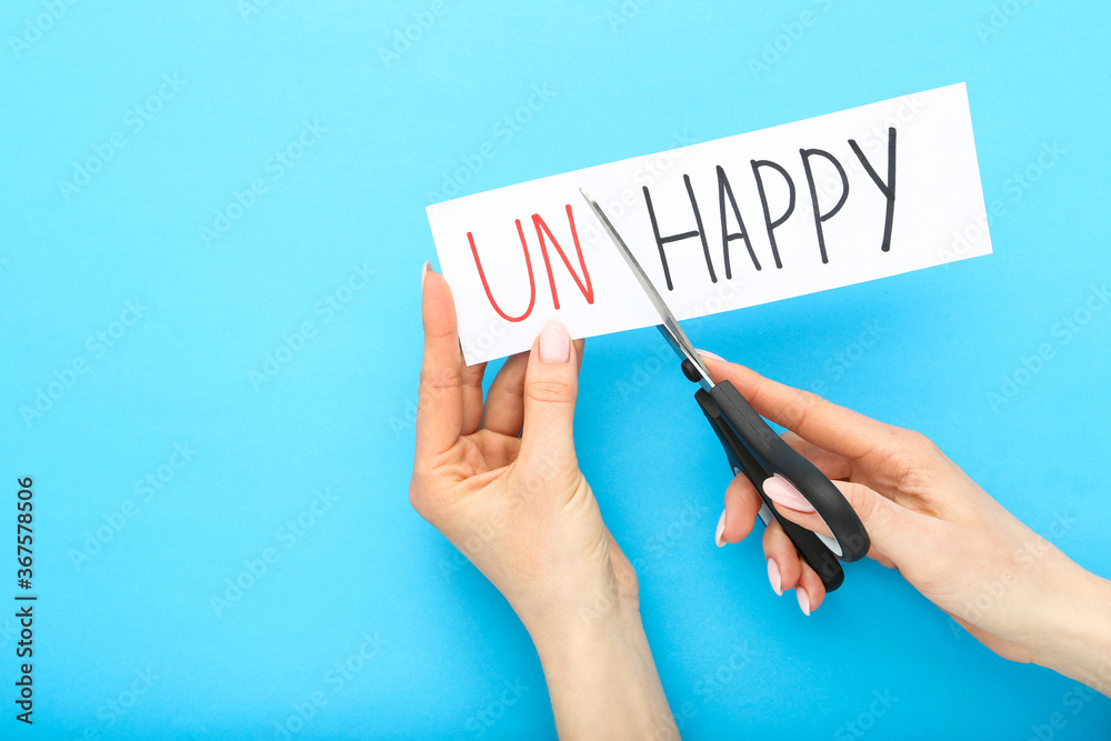 Female hands using scissors for cutting word Unhappy Female hands using scissors for cutting word Unhappy