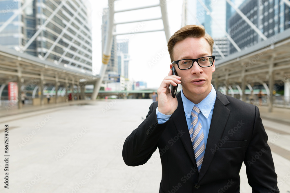 Young handsome blond businessman talking on the phone in the city outdoors Young handsome blond businessman talking on the phone in the city outdoors