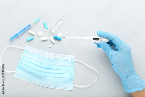 Medicine mask with pills, syringe and thermometer on grey background