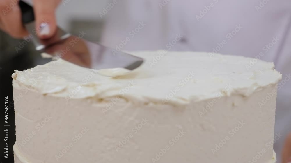Close-up of the pastry chef aligns the top of the cake with butter cream using a metal spatula. The process of preparing a delicious cake in a professional pastry shop. Slow motion. Close-up of the pastry chef aligns the top of the cake with butter cream using a metal spatula. The process of preparing a delicious cake in a professional pastry shop. Slow motion.