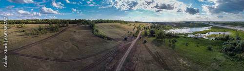 Panoramic aerial landscape view from above, green grass field, green forest, small lake and gravel roads during summer day in countryside near Samara city, Russia