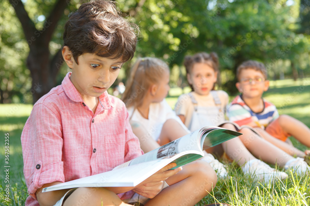 Cute little boy looking overwhelmed, reading a book at public park Cute little boy looking overwhelmed, reading a book at public park