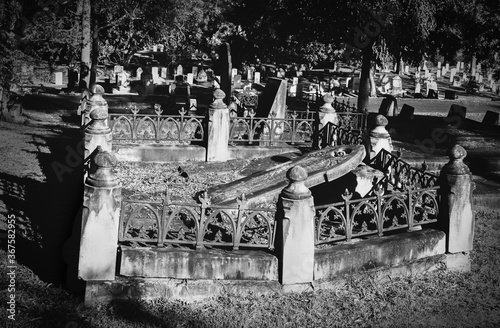 Old broken grave with crumbling fallen tombstone and decaying wrought iron fence around it in dark and gloomy cemetery