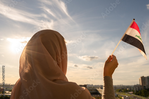 Silhouette of muslim woman in head scarf with Iraq flag at blue sunset sky. Concept of freedom