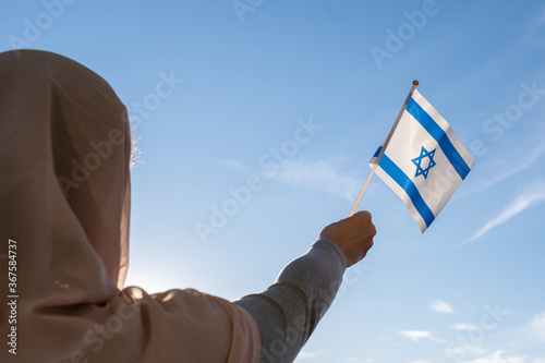 Silhouette of muslim woman in head scarf with Israel flag at blue sunset sky. Concept of freedom