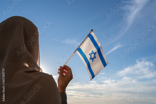 Silhouette of muslim woman in head scarf with Israel flag at blue sunset sky. Concept of freedom