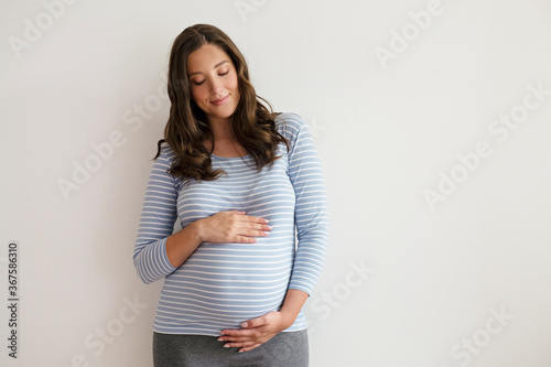 Portrait shot of young beautiful woman on third trimester of pregnancy. Close up of pregnant female with arms on her round belly. Expecting a child concept. Background, copy space. photo