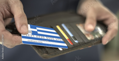 Man pulls plastic bank card with flag of Greece out of his wallet, fictional card number