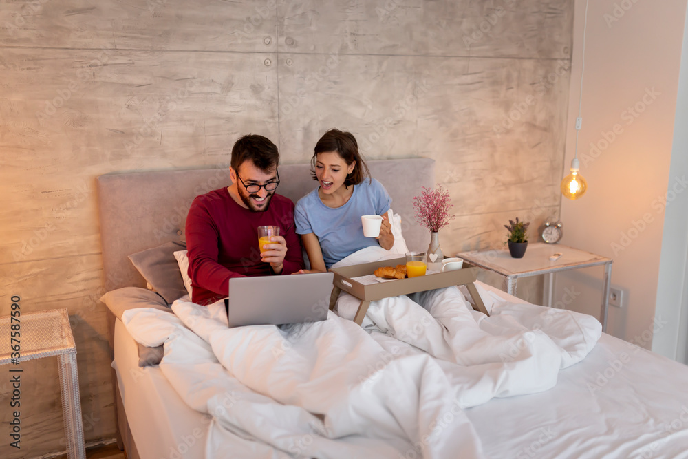Couple using laptop computer and having breakfast in bed