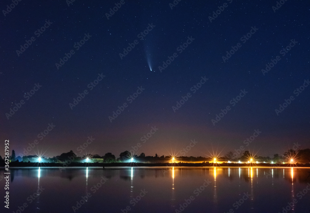 Comet NEOWISE in the night sky over the river, with the Milky Way and a tourist with a tent