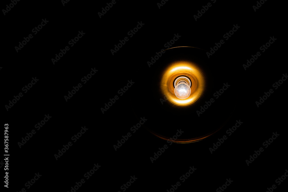 Bombilla encendida en lámpara dorada y fondo negro Bombilla encendida en lámpara dorada y fondo negro