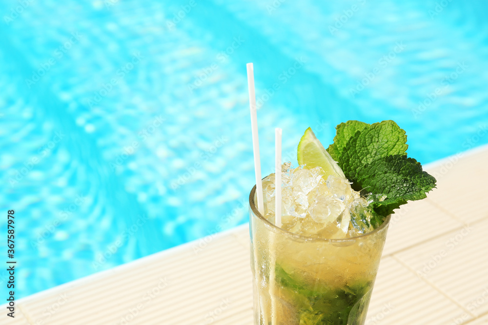 Glass of delicious mojito near swimming pool, space for text. Refreshing drink - obrazy, fototapety, plakaty 