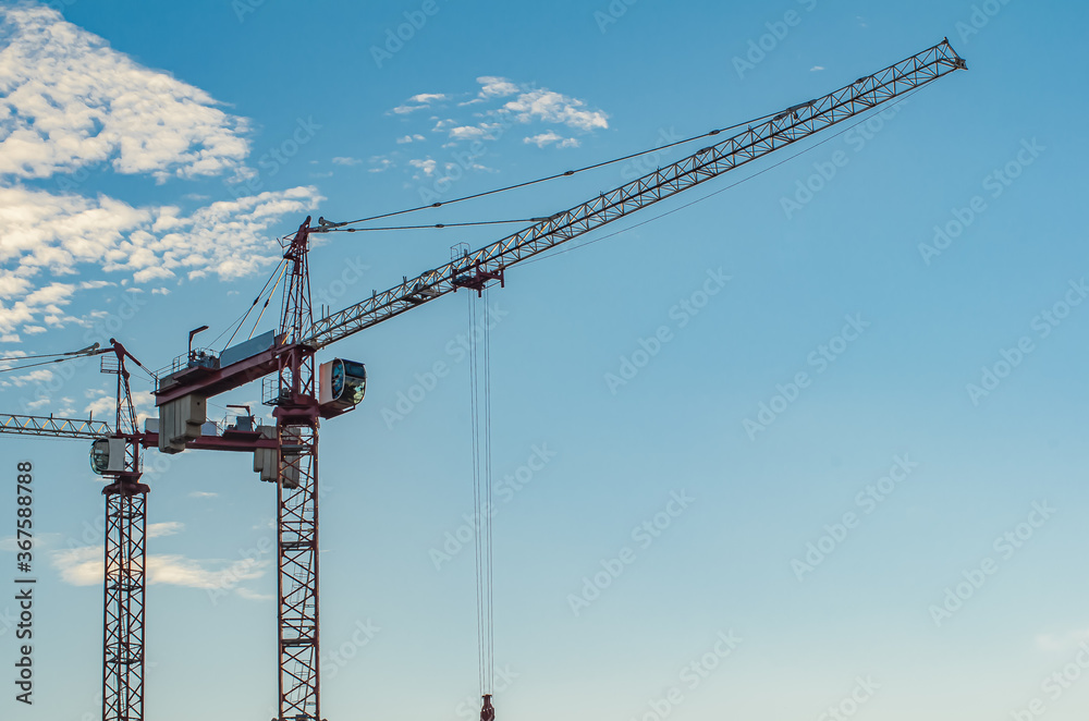 Two high-rise red construction cranes against the blue sky. Construction business, technologies and machines. Two high-rise red construction cranes against the blue sky. Construction business, technologies and machines.