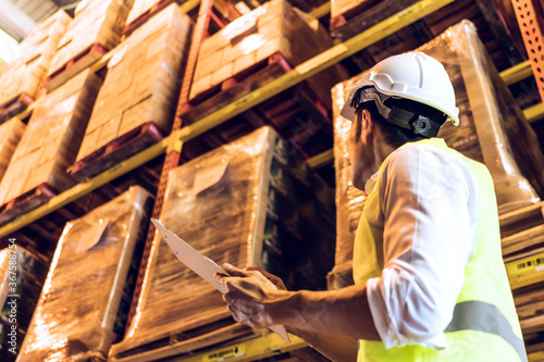 Asian man worker holding paper chart checking stock inventory at logistic warehouse storage. side view of male employee working for business export import or shipping company. copy space 