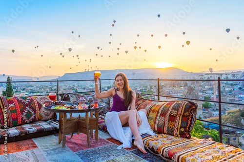A woman have breakfast on one of the Cappadocia roof in early morning sunrise, when balloons fly. Romantic scene Cappadocia, Turkey.
