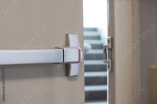 Emergency fire exit door. Closed up latch and rusty door handle of emergency exit. Push bar and rail for panic exit. Open one way door. steel of handle for the white door fire exit