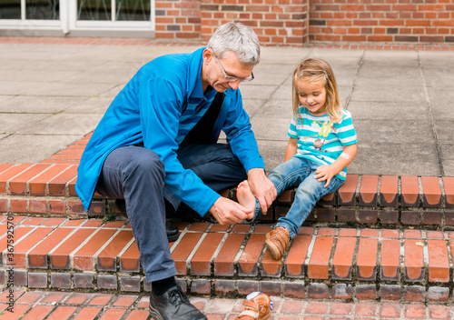 Mature man tickling foot of toddler girl while cleaning shoes photo