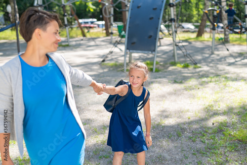 The naughty girl pulls her mother by the hand, wanting to stay on the playground. The capricious daughter resists and does not want to leave.