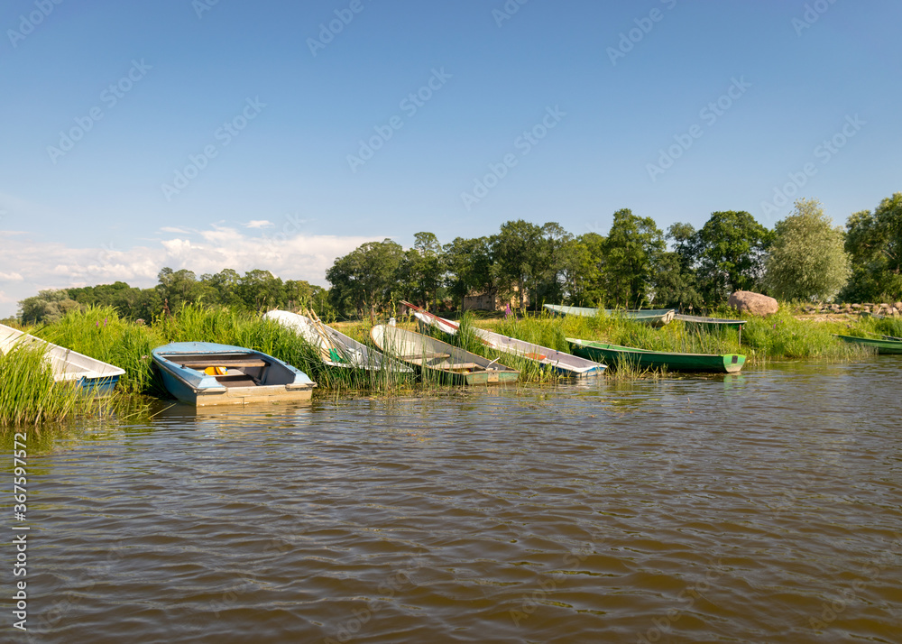 summer landscape with boats on the shore of the lake, the shore is covered with green grass, reflections in the water