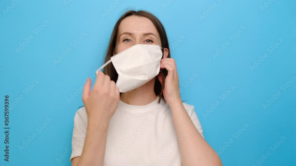 Portrait of young brunette woman in white medical mask pose on blue studio background, taking off protective face mask breathing deeply feels good. Quarantine end, world defeated COVID-19 concept Portrait of young brunette woman in white medical mask pose on blue studio background, taking off protective face mask breathing deeply feels good. Quarantine end, world defeated COVID-19 concept