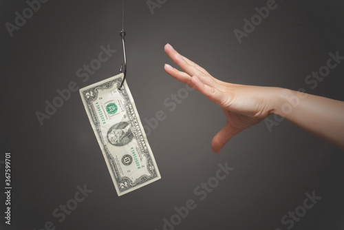Female hand is trying to catch a dollar currency which hanging on the fish hook. Financial trap.