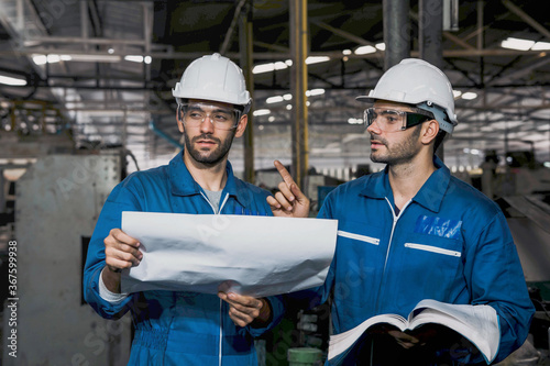 Factory Engineer or mechanical worker with white safety helmet holding the manual and checking on production in a factory. Industrial,Warehouse Heavy Mechanic, Engineering Concept. 
