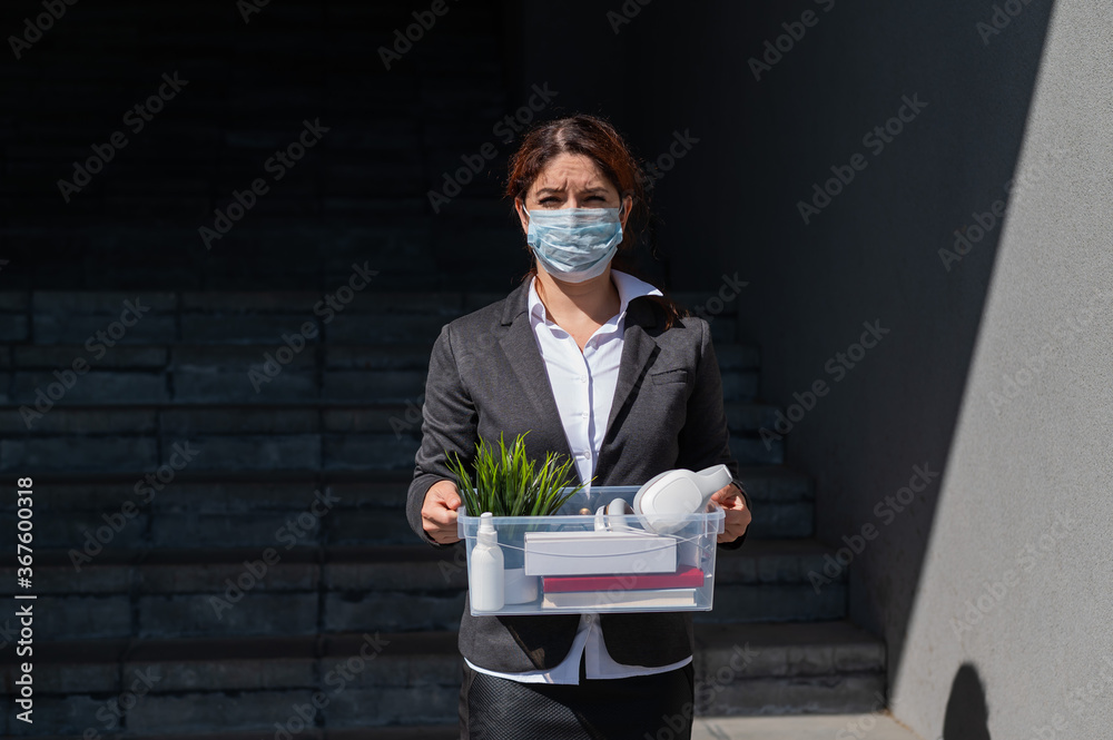 Φωτογραφία unemployed woman in a protective mask is standing with a box of personal belongings at the stairs