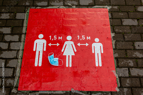 A crumpled protective mask lies on a red sign that informs people to keep a social distance. Sign informing people to keep 1,5 meter distance from each other, prevent spreading Coronavirus infection. photo