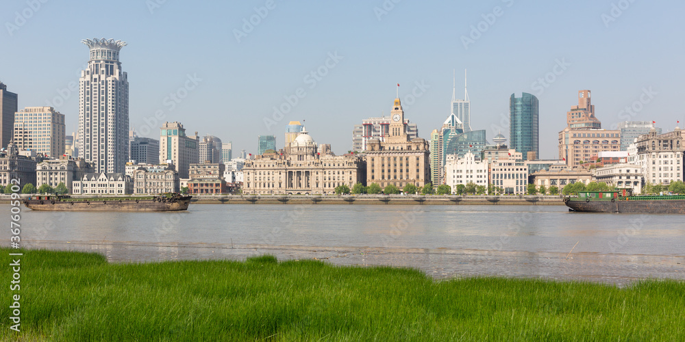 Shanghai, China - April 19, 2018: Panorama of the Bund with green grass and Huangpu River in the foreground. Historical buildings of Shanghai. Shanghai, China - April 19, 2018: Panorama of the Bund with green grass and Huangpu River in the foreground. Historical buildings of Shanghai.