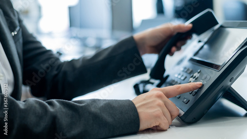 Closeup female hand on landline phone in office. Faceless woman in a suit works as a receptionist answering the phone to customer calls. photo