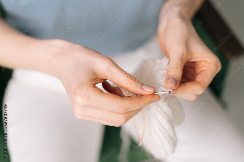 Close up of hands of unrecognizable woman knitting handmade clothes with spokes using white wool yarn. Concept of leisure activity.