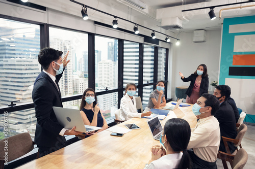 Businessman wearing face mask with presentation of business plan on laptop, corporate business meeting in modern office