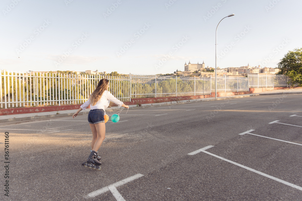 Blonde girl in white blouse, jeans and colored balloons skating in the city. Roller-skating concept Blonde girl in white blouse, jeans and colored balloons skating in the city. Roller-skating concept